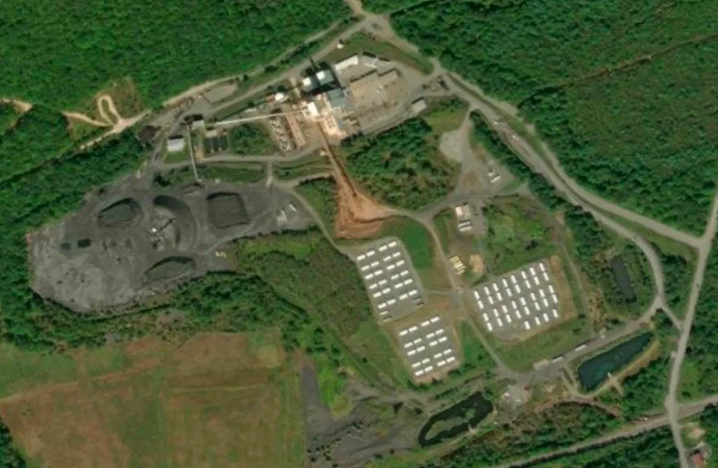 Aerial satellite image from PA state Parks, Forests and Geology Interactive Map showing a power plant, coal waste heaps, and various power plant industrial equipment and some buildings and vehicles in a network of little roads surrounded by forest with trees.
